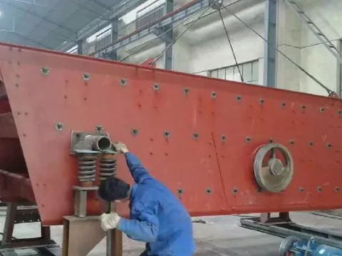 A worker beside a red vibrating-screen assembly in the workshop.